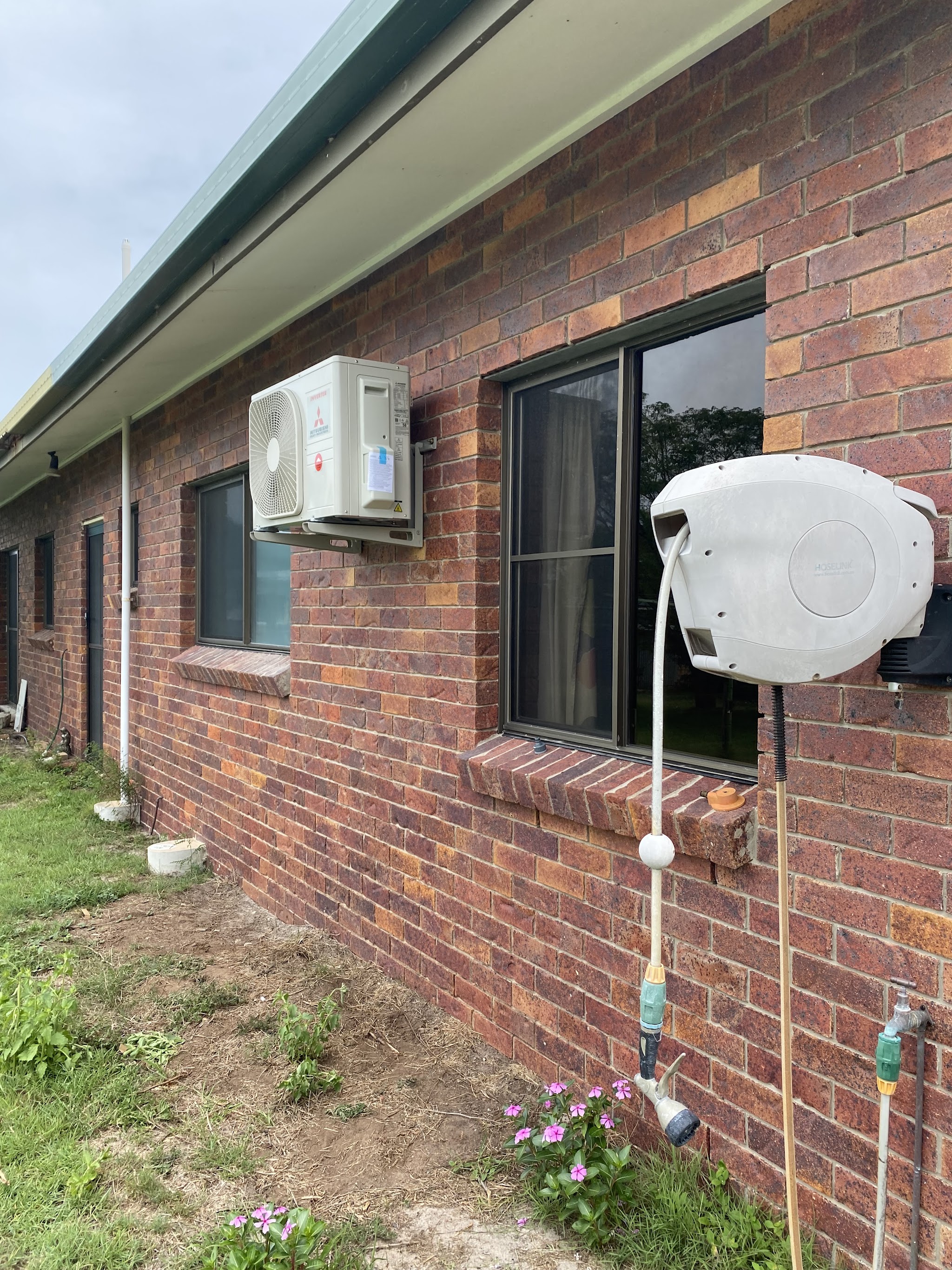 A Mitsubishi Electric inverter outdoor unit mounted on wall brackets against brickwork under the eaves