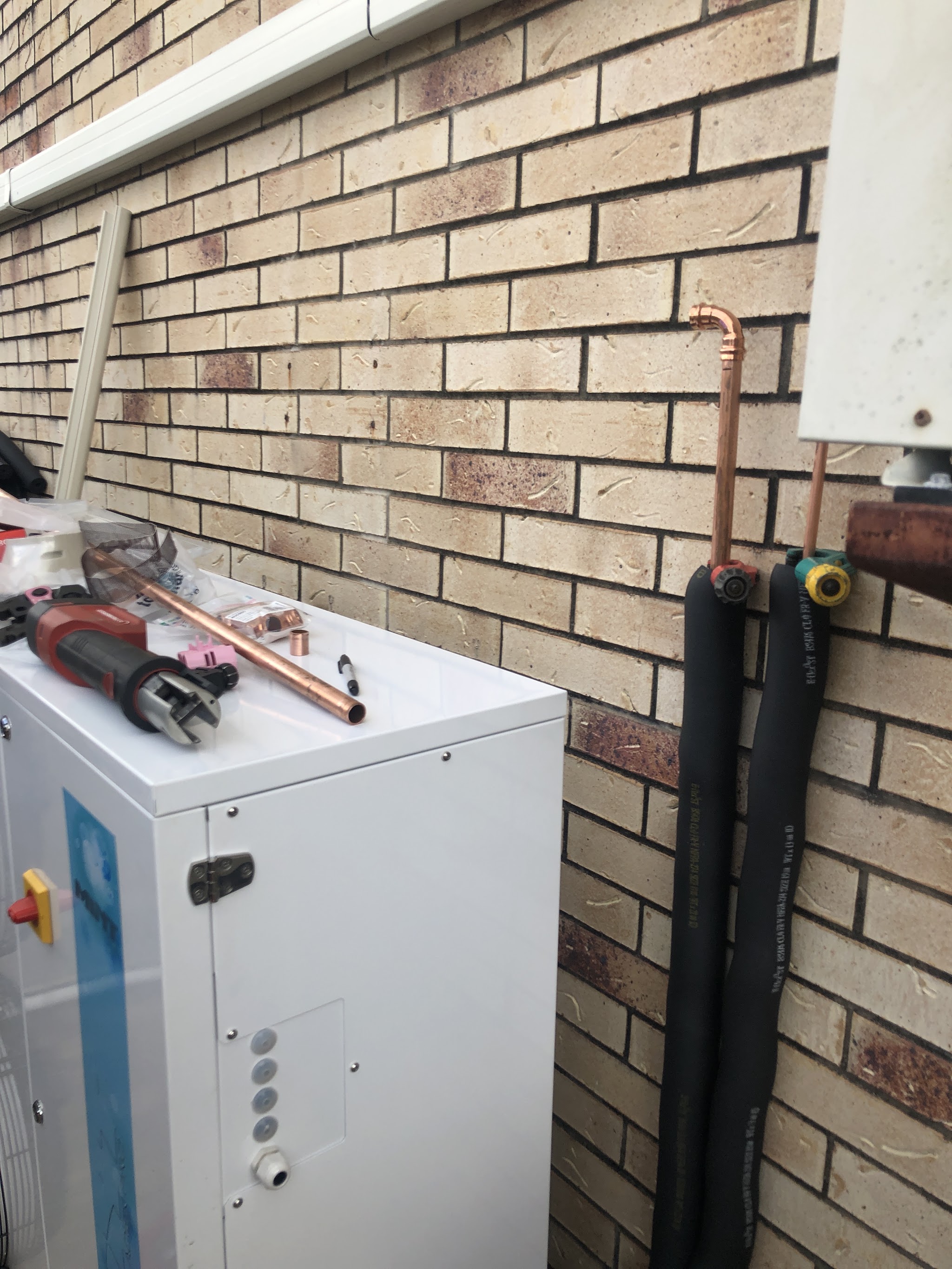 Copper pipe, a pipe cutter and press tool laid on a new unit, with insulated refrigerant lines running up a brick wall